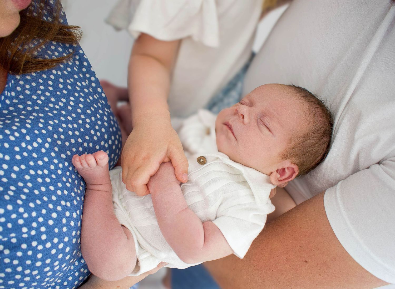 A sleeping newborn baby wearing white clothing rests peacefully on blue polka dot bedding.