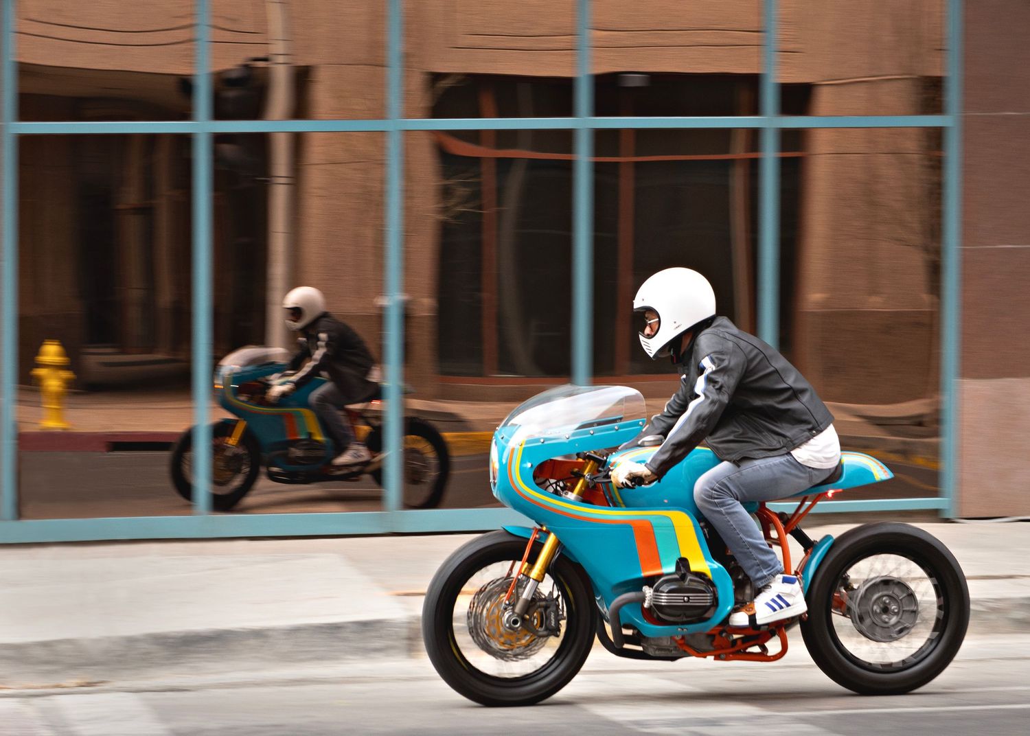 Riders racing vintage-style turquoise motorcycles on urban street.