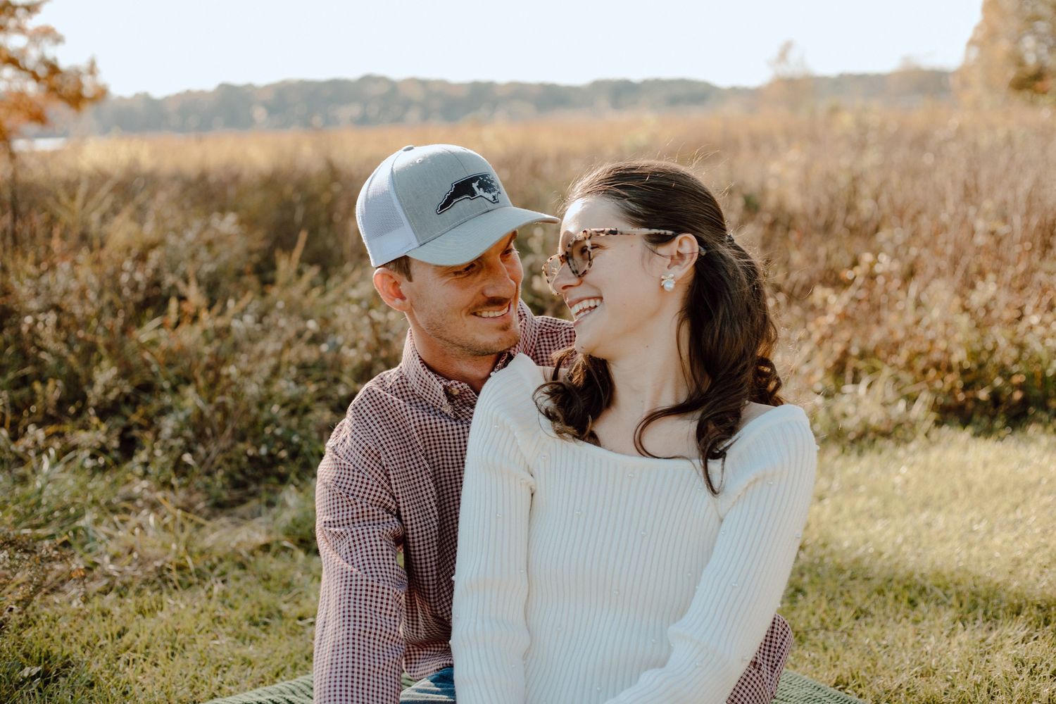 A couple in casual attire shares a tender moment in a sunlit field during autumn.
