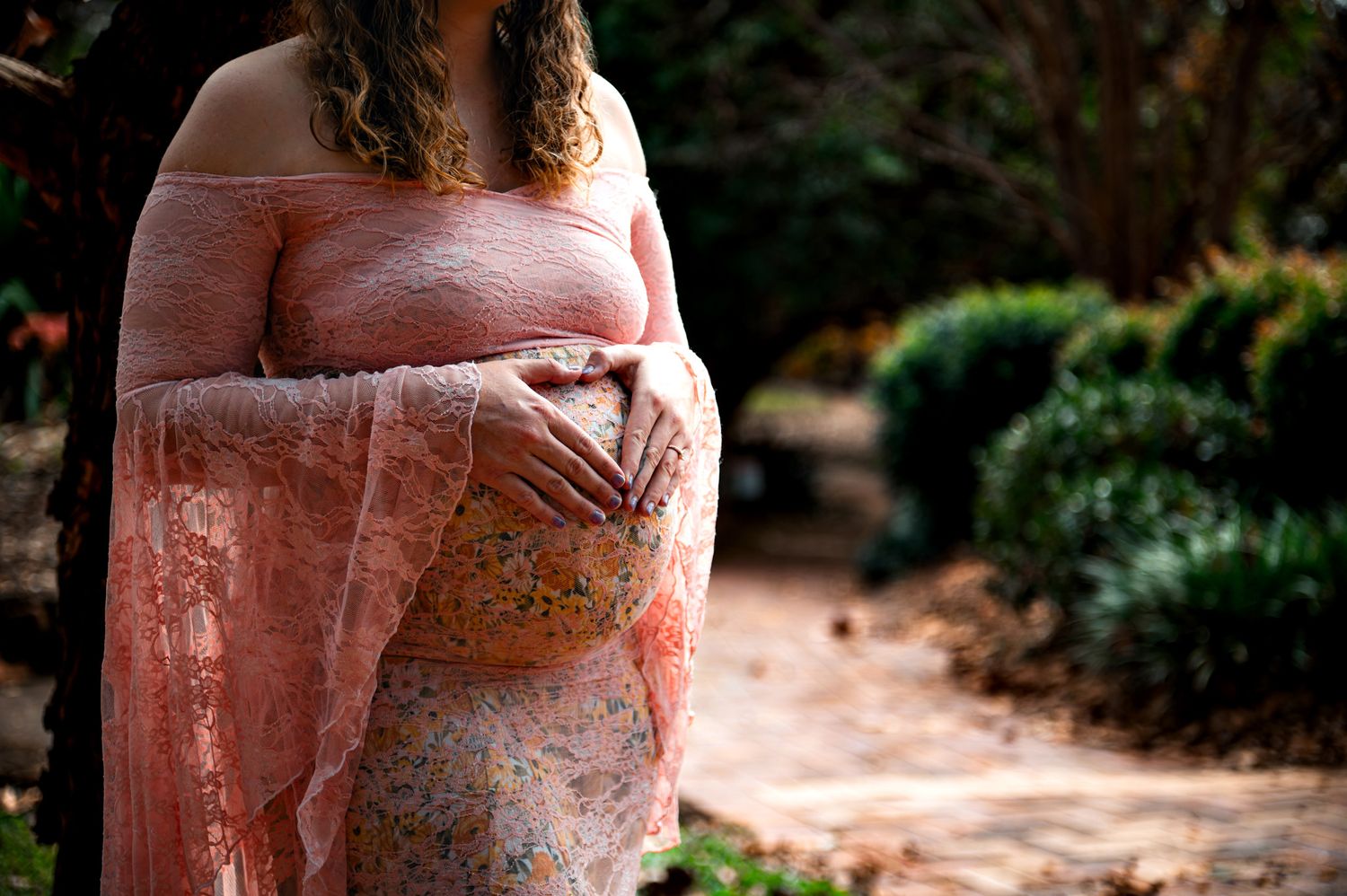 Maternity photography in a garden setting with soft pink tones and natural light.