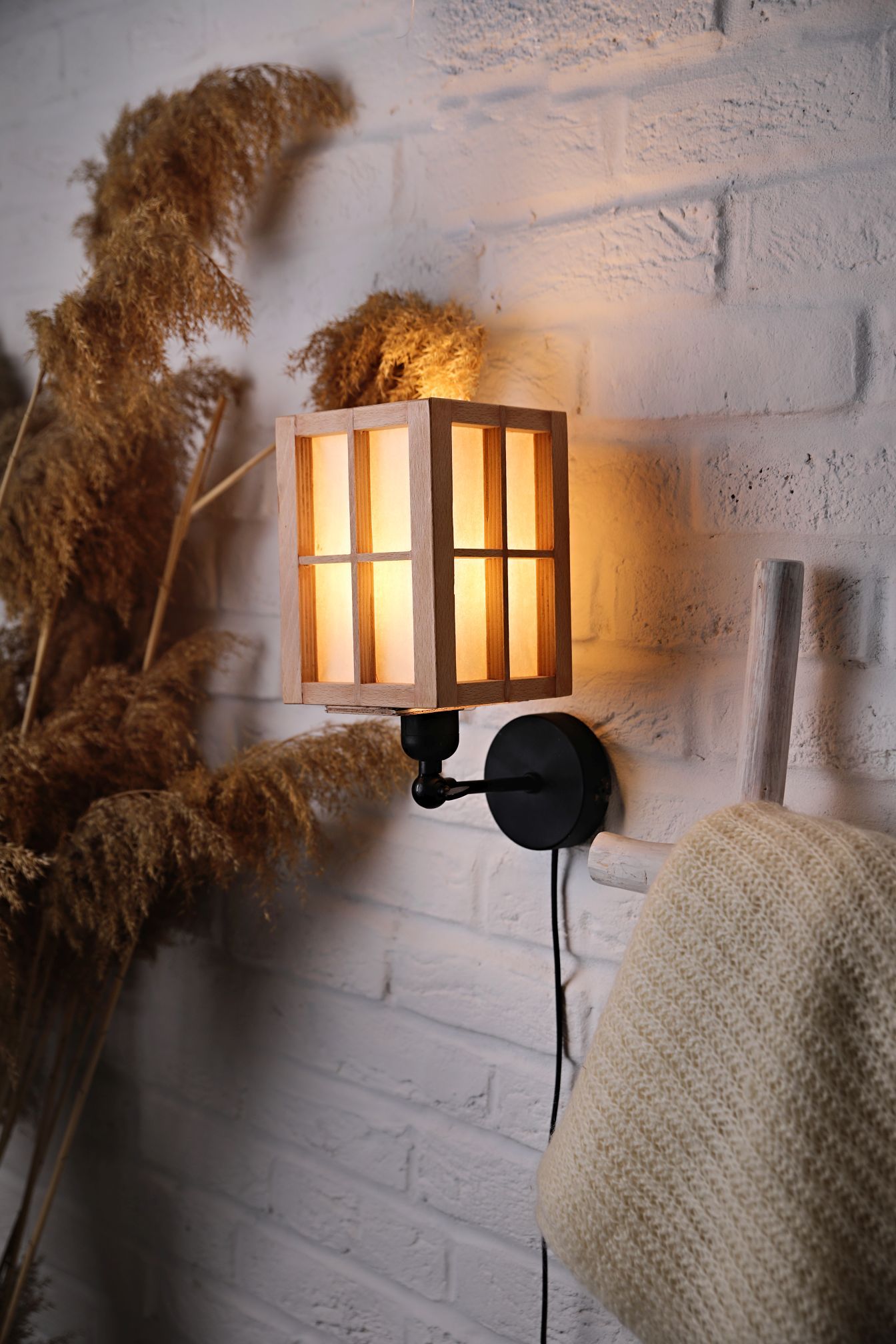 Cozy wall sconce lamp glowing next to dried pampas grass against white brick wall.