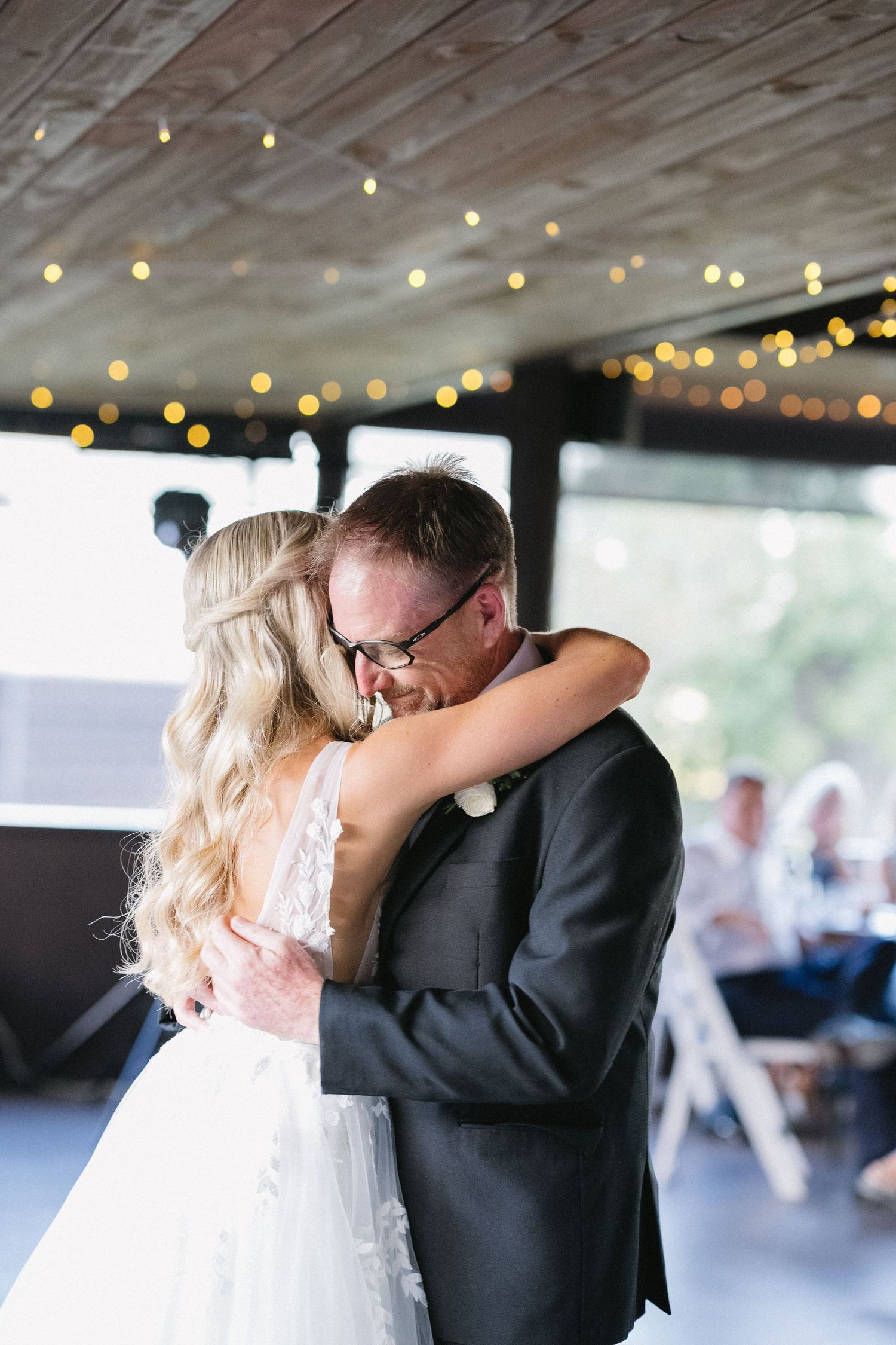 A tender moment shared during their first dance under twinkling string lights at a rustic reception.