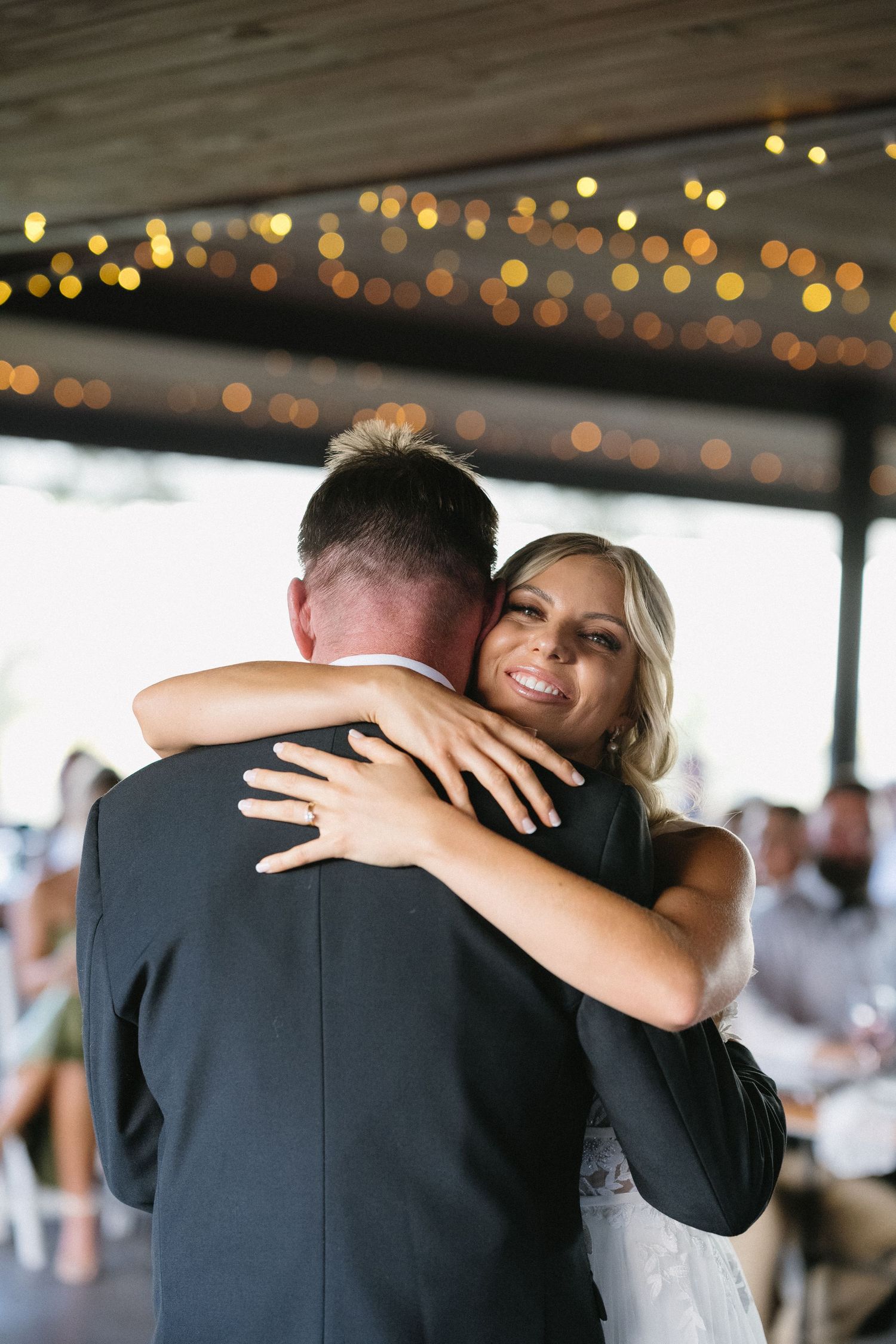 Bride and groom share emotional embrace during first dance under twinkle lights.