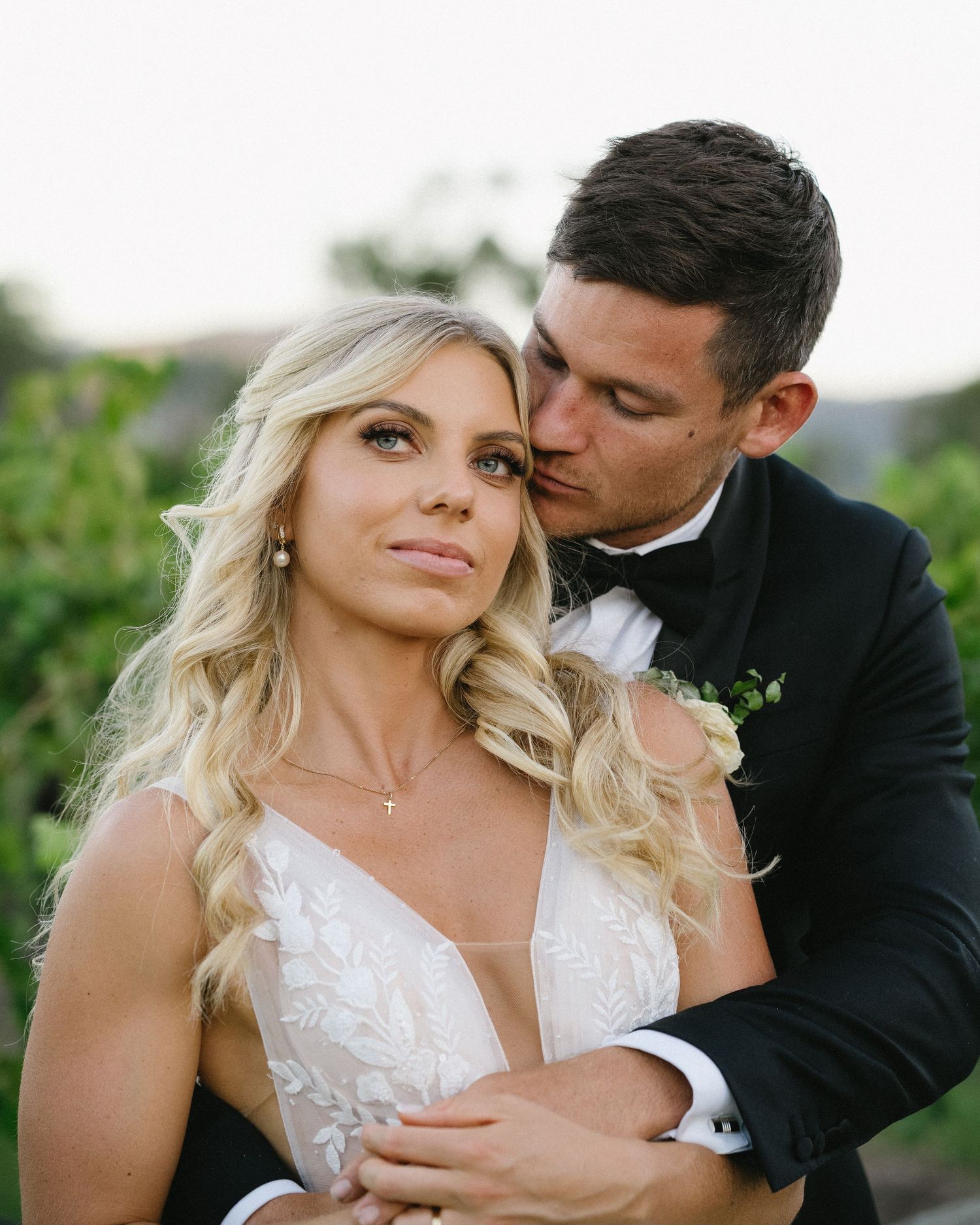Intimate romantic moment between newlyweds in formal attire against natural backdrop.