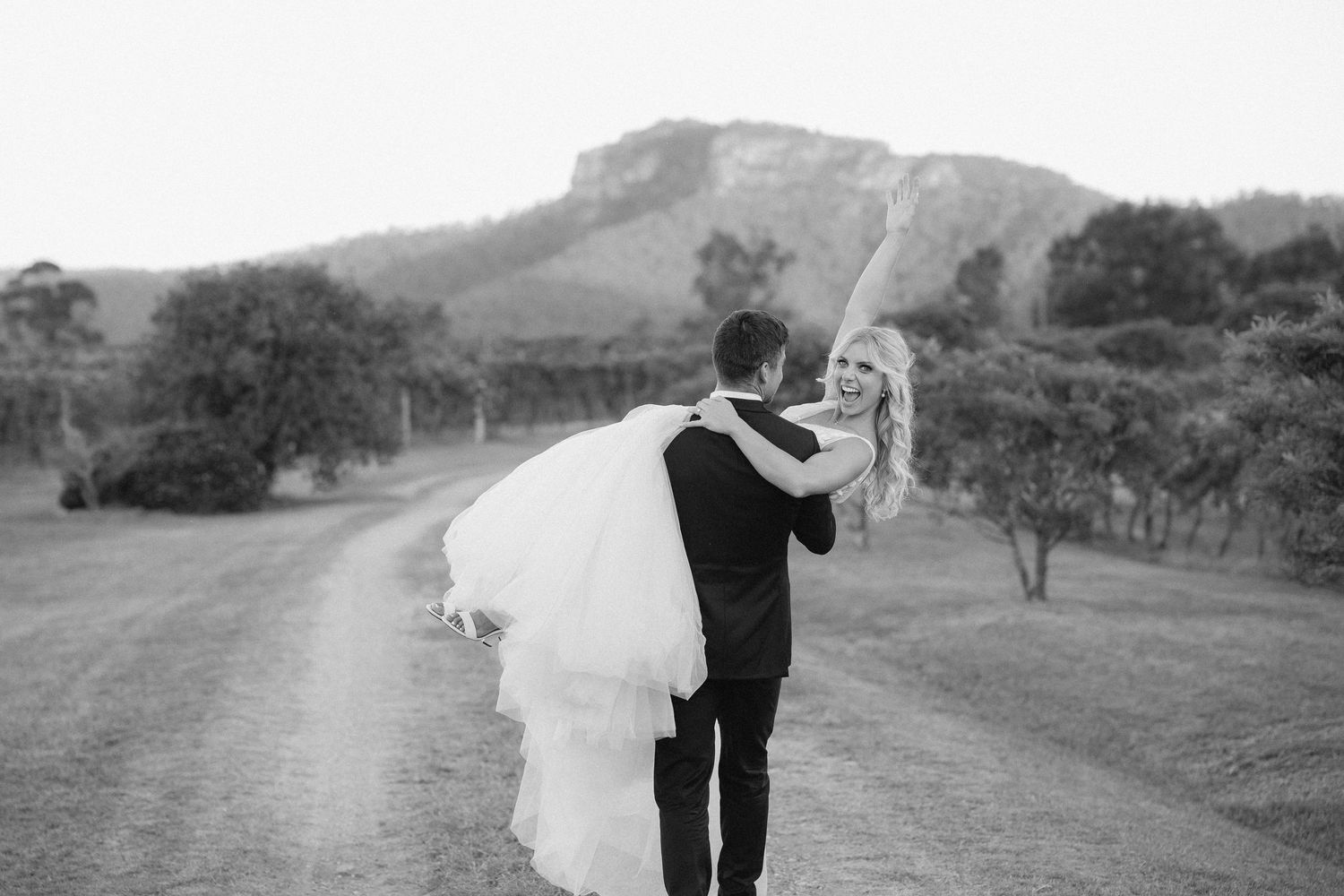 Romantic wedding couple embrace on a country road with rolling hills in black and white photography.