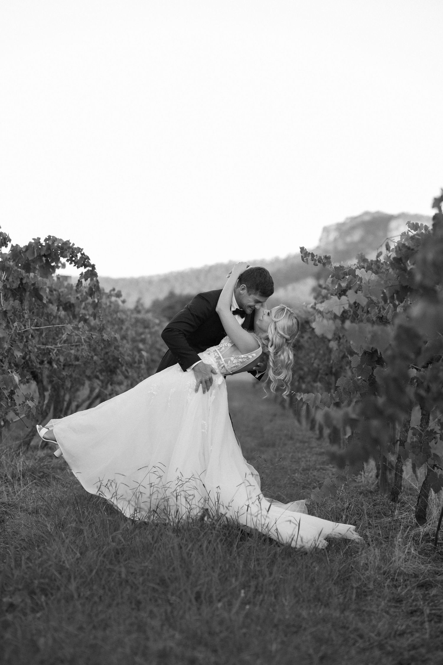 Romantic black and white photo of newlyweds sharing an intimate moment in a vineyard.