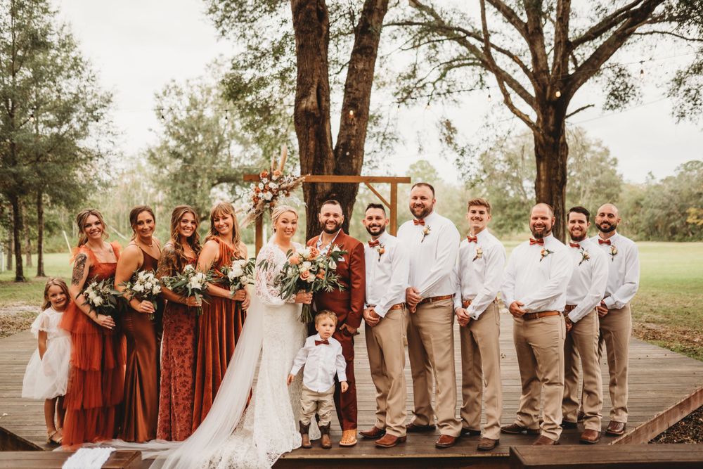 Wedding party poses on wooden deck with bridesmaids in rust-colored dresses and groomsmen in khaki.