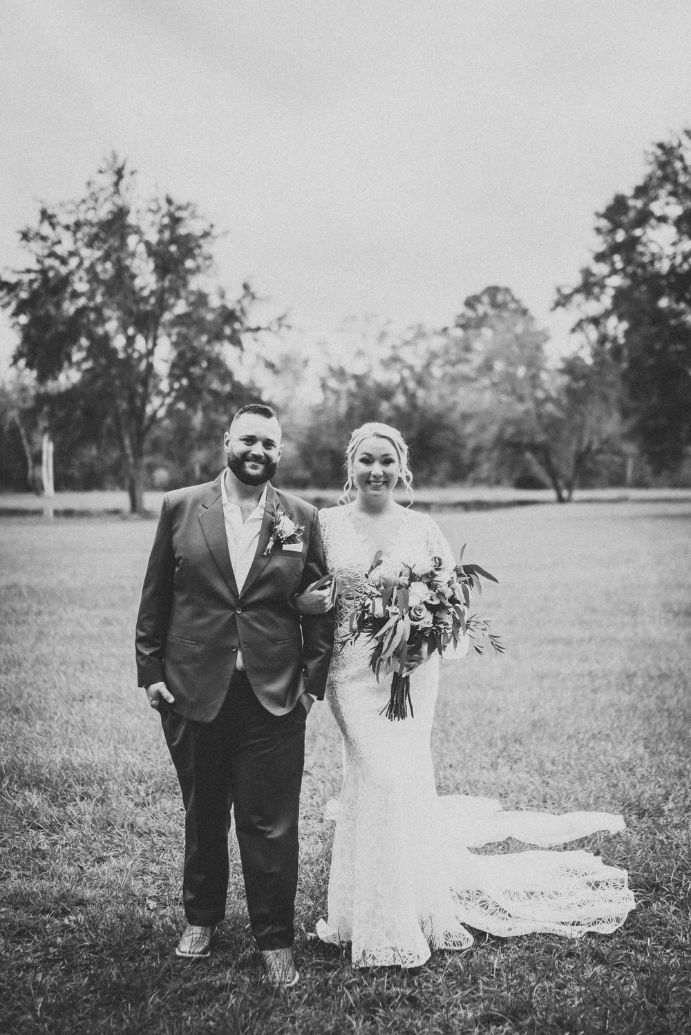 Black and white portrait of newlyweds standing together in an outdoor garden setting.