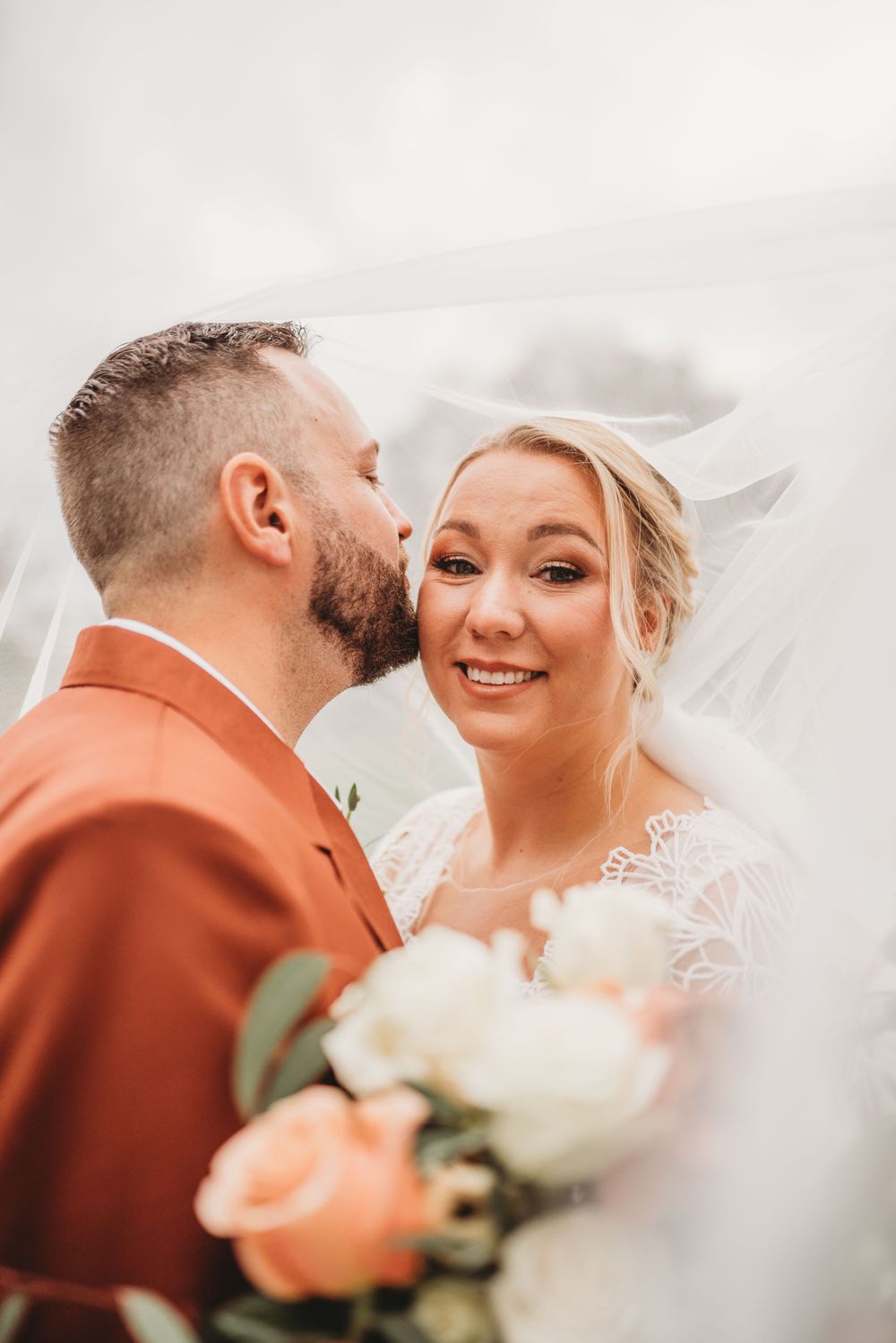 Romantic close-up of wedding couple with peach roses and flowing veil.