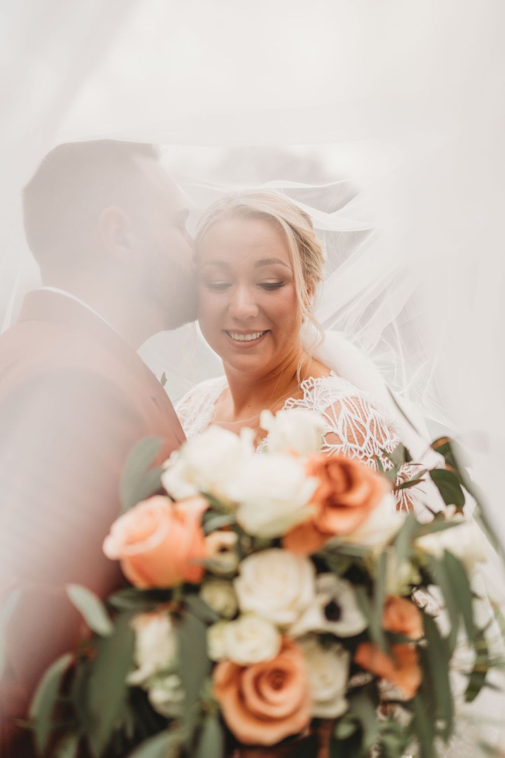 Dreamy wedding portrait with soft lighting highlighting peach and white roses.