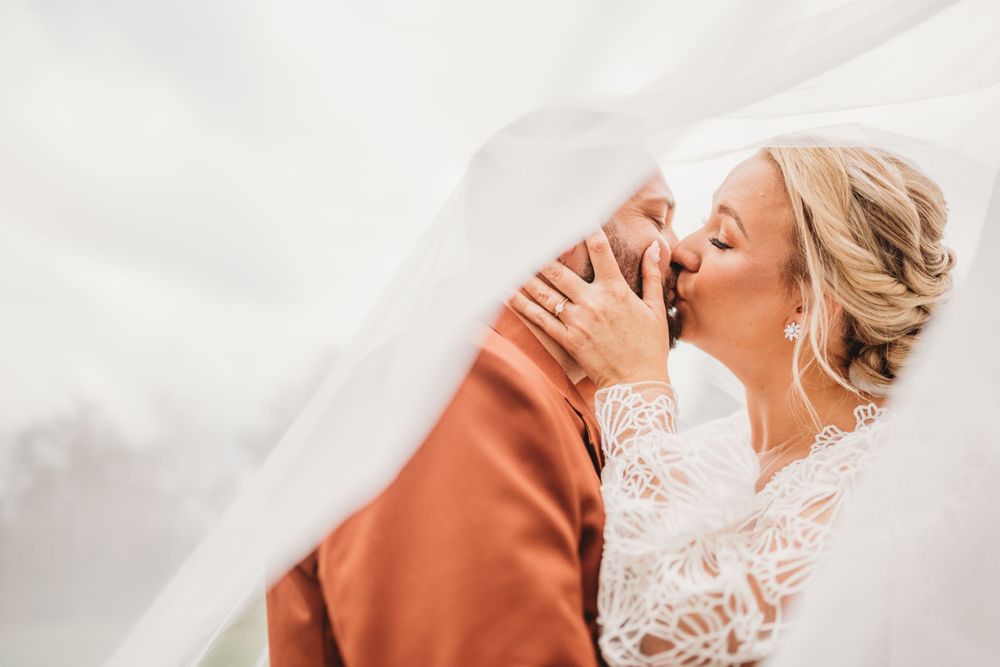 Artistic wedding photo through sheer veil showing rust suit and lace dress details.