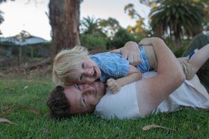 Parent and child sharing a playful moment lying on grass outdoors.