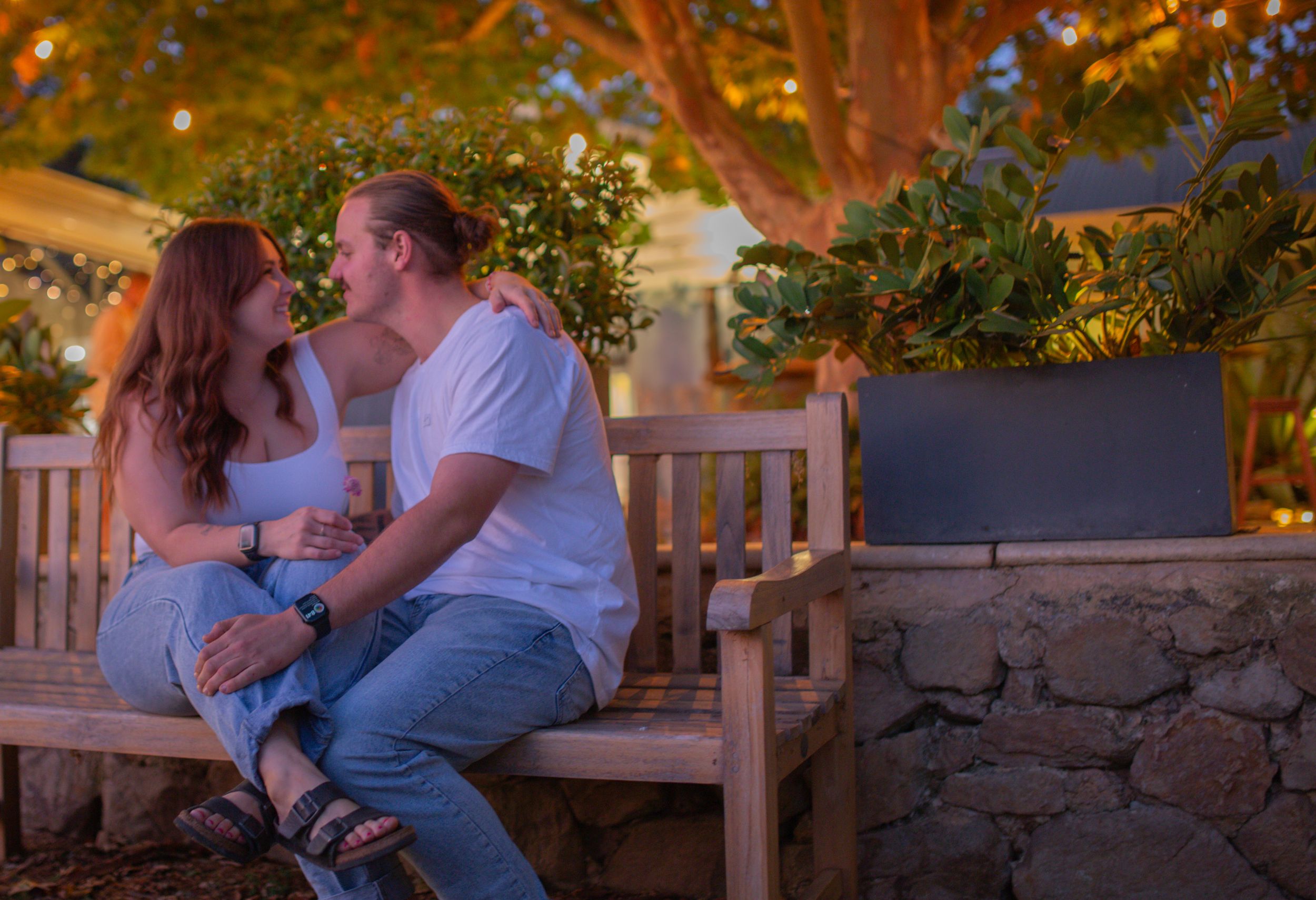 Couple sharing an intimate moment on a wooden bench at dusk surrounded by garden lighting.