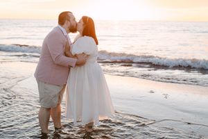 A couple shares a romantic moment on a beach at sunset with waves crashing in the background.