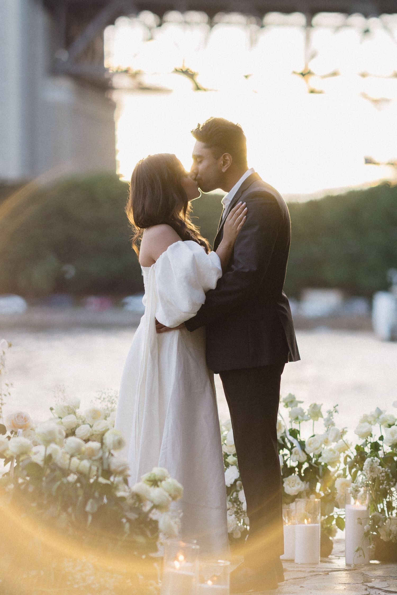 A romantic outdoor wedding ceremony at sunset with white floral decorations and soft golden light.