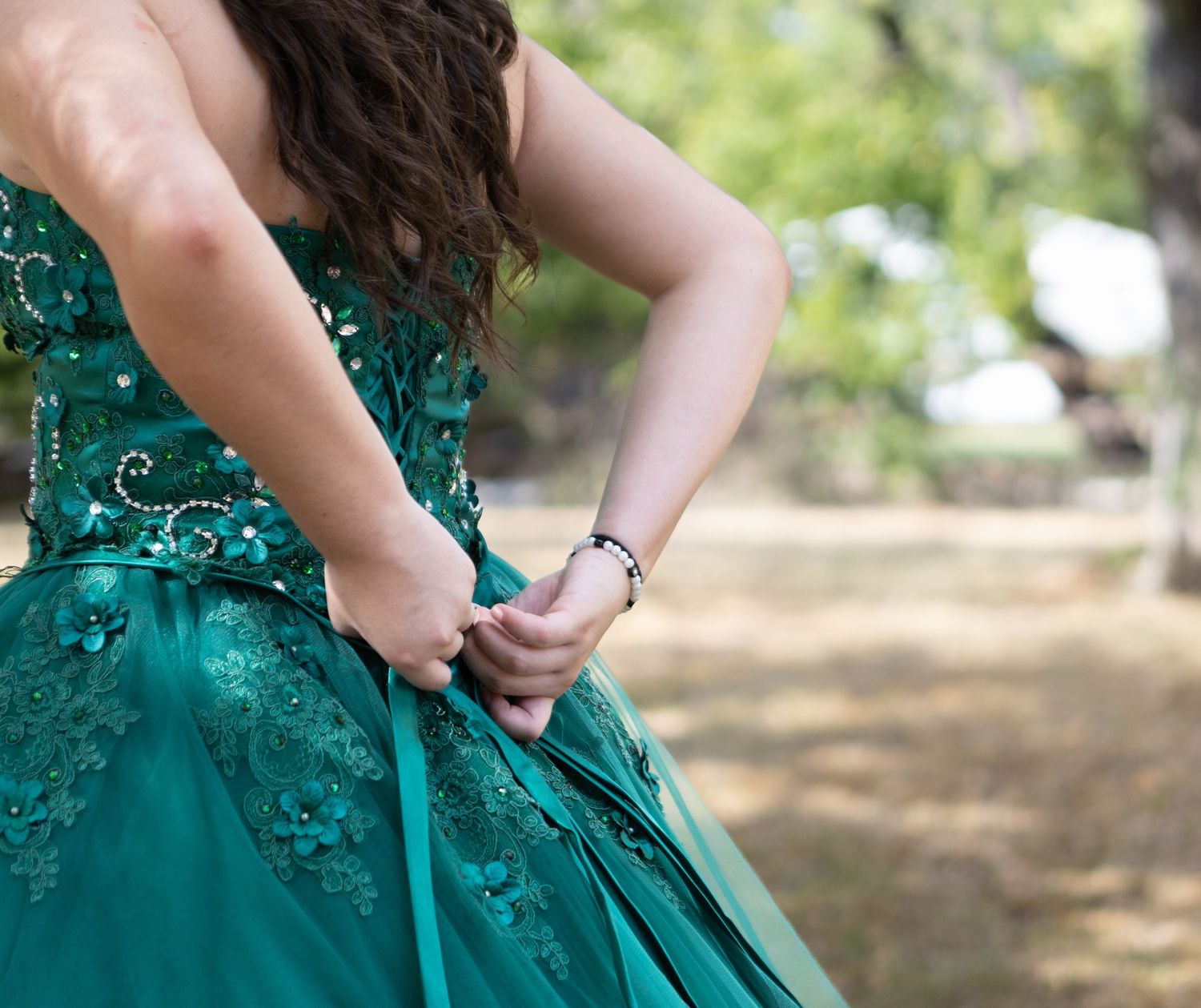 Detailed close-up of teal gown showing intricate beadwork and lace appliques.