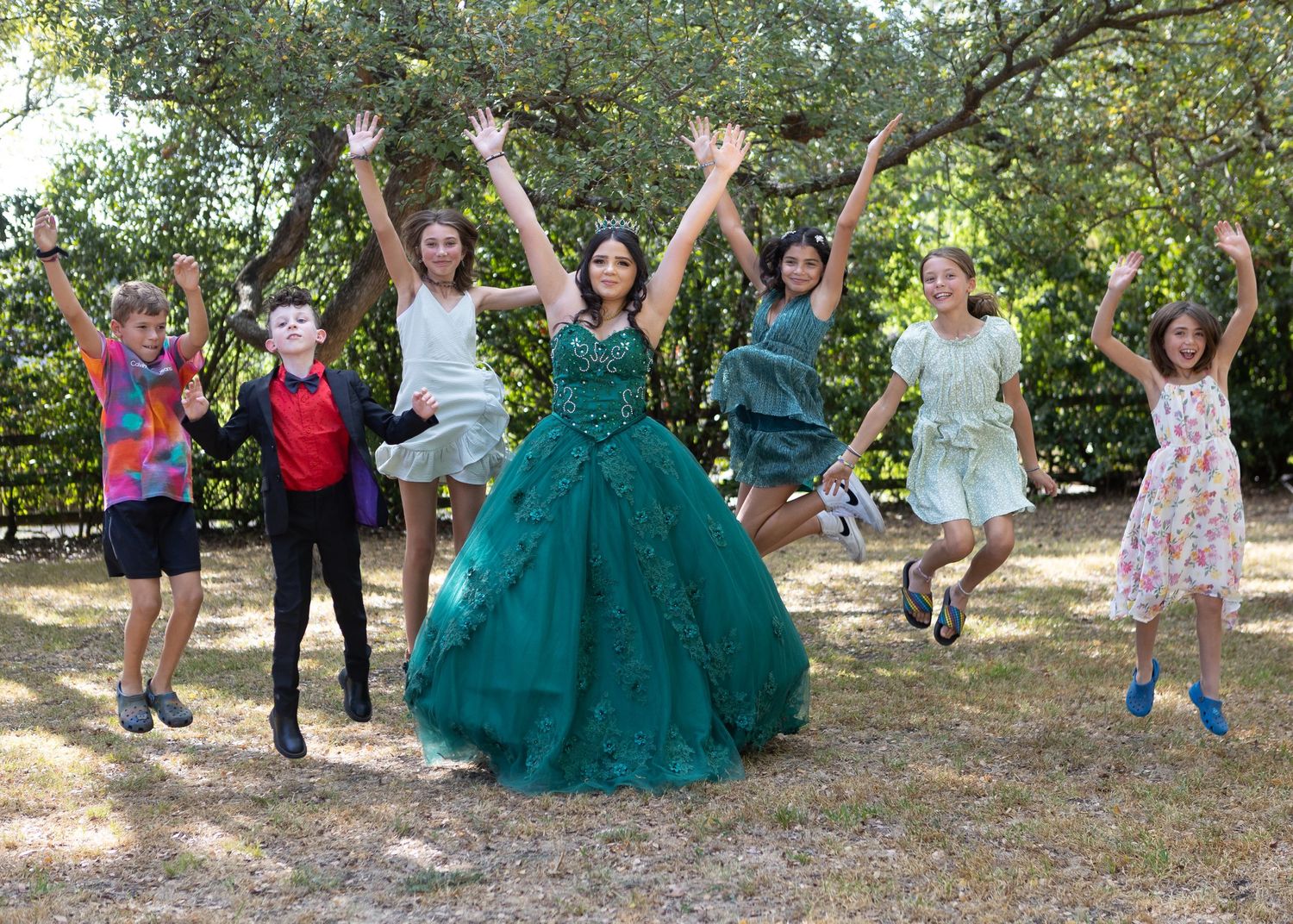 Group of friends jumping and celebrating outdoors with a person wearing an emerald green ballgown.