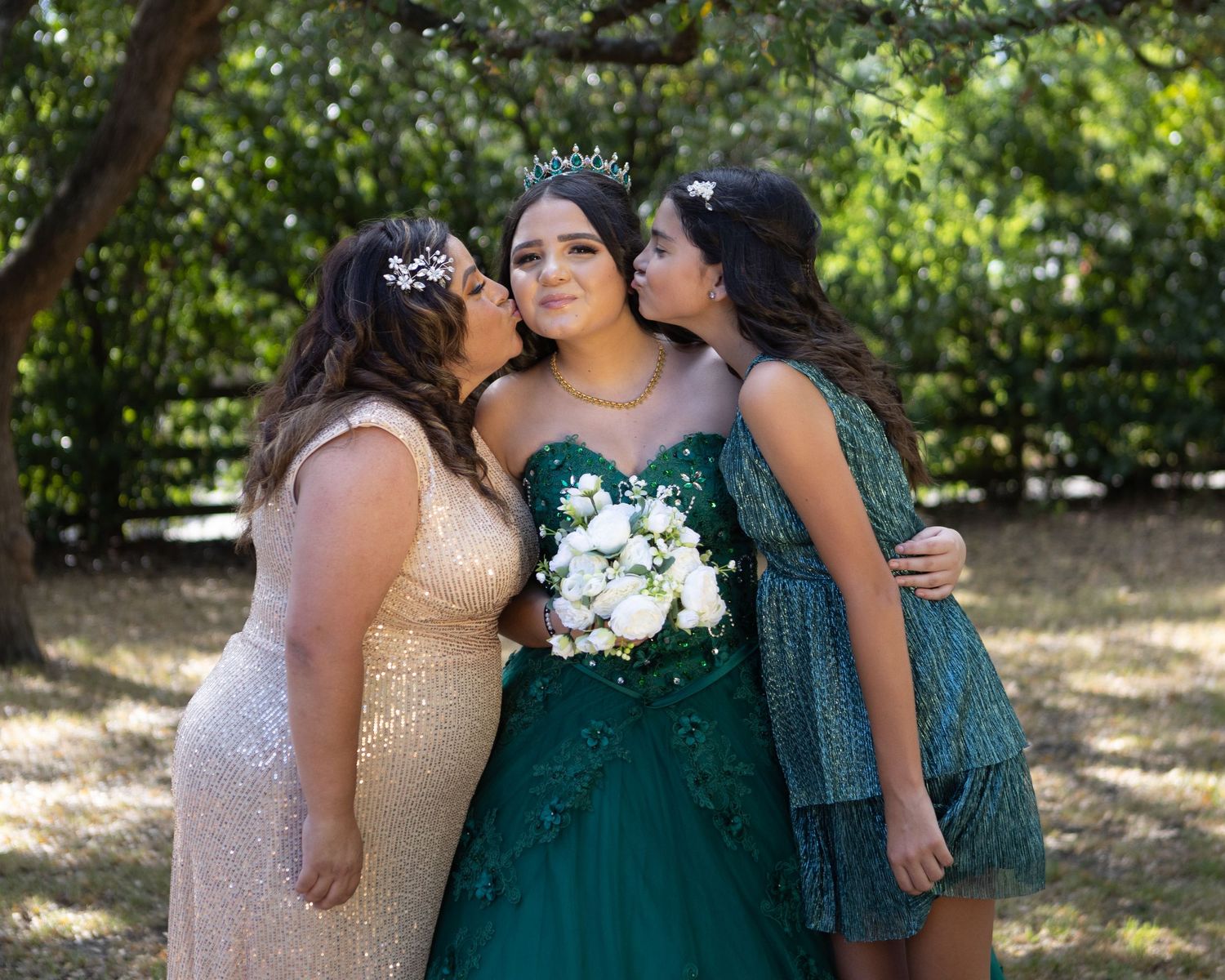 Three attendees share an intimate moment at a celebration with the central figure wearing emerald green.