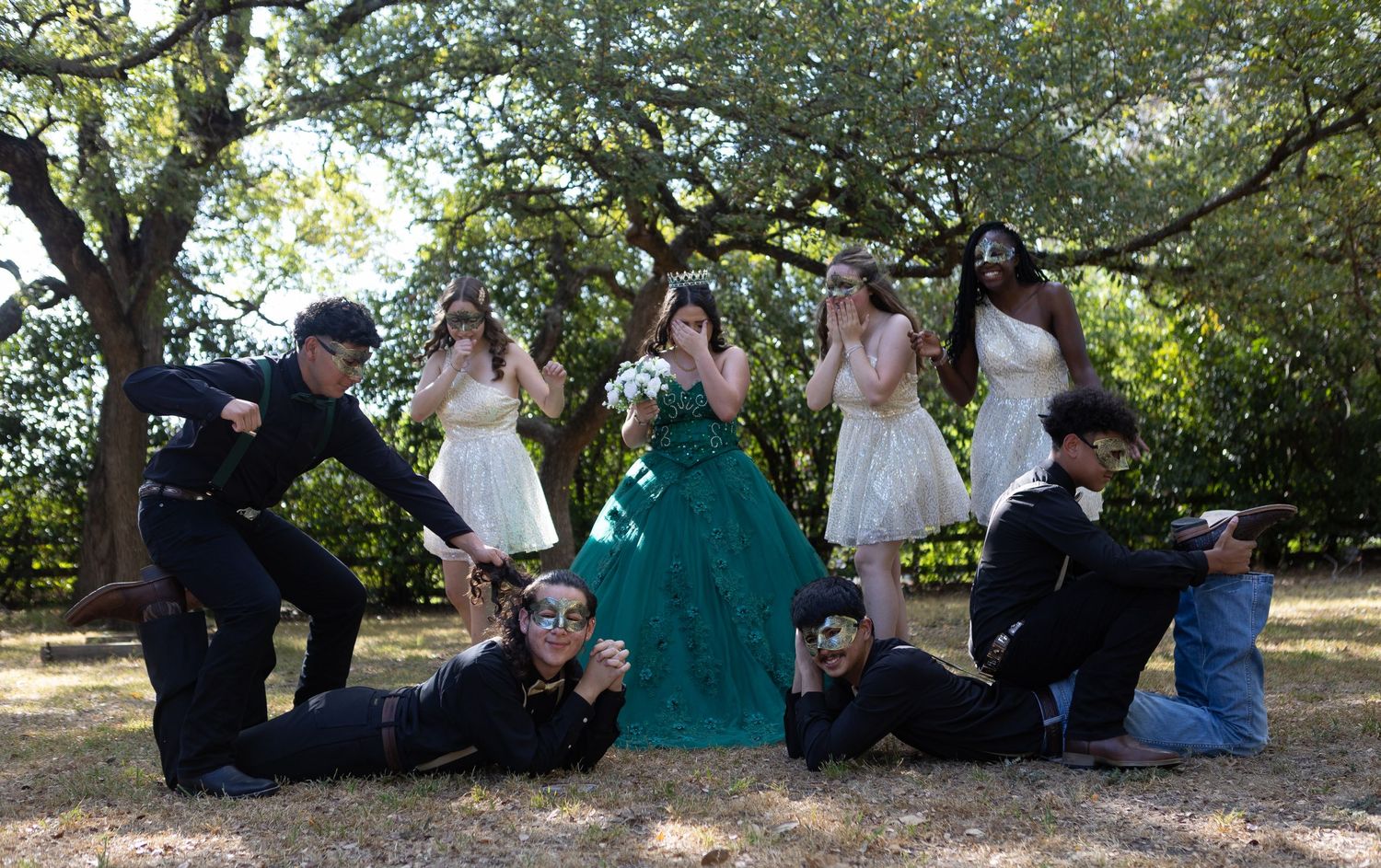Creative group photo with celebrants posing dramatically on ground around person in emerald gown.