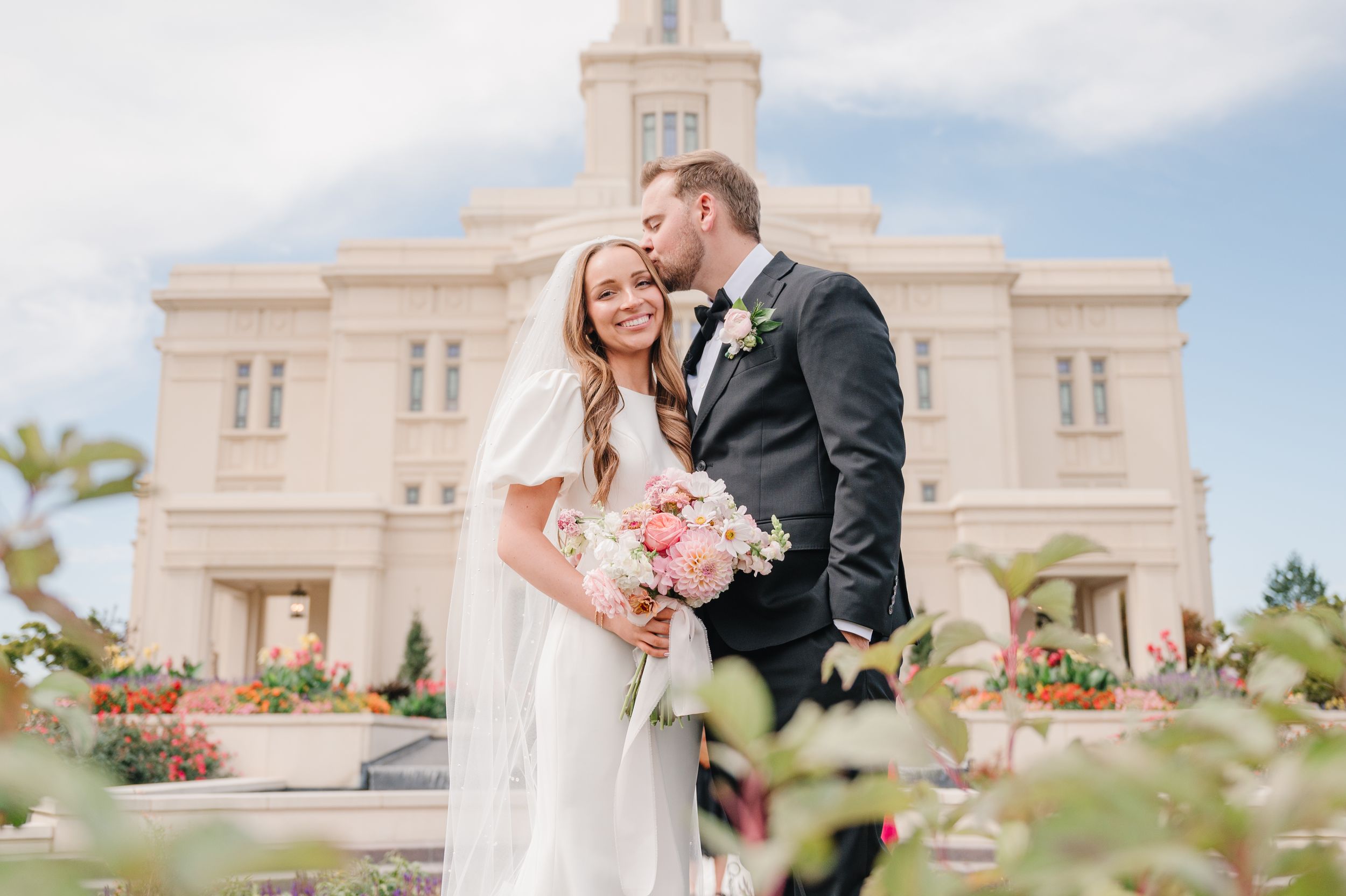 A wedding portrait in front of an elegant white temple building with beautiful gardens.