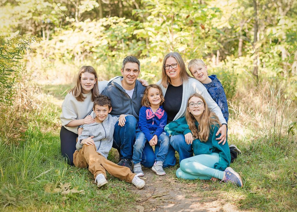 A group sits casually together outdoors in a wooded setting wearing coordinated blue and white clothing for a photo session.