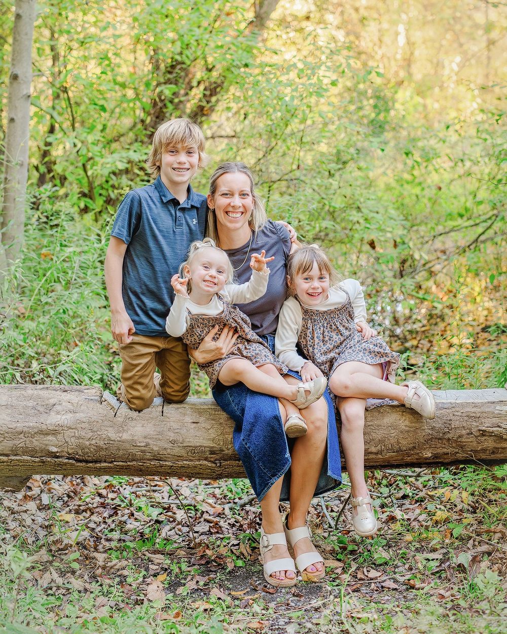 Family members sit together on a fallen log in a sunlit wooded area during an outdoor photo session.