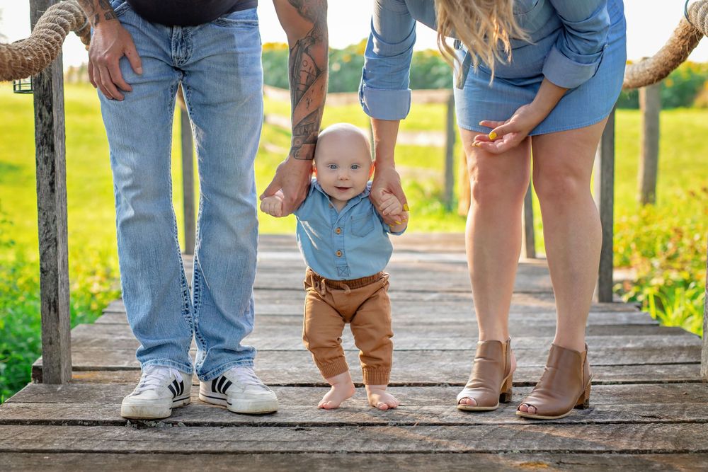 Family walking together on wooden bridge path through sunlit meadow.