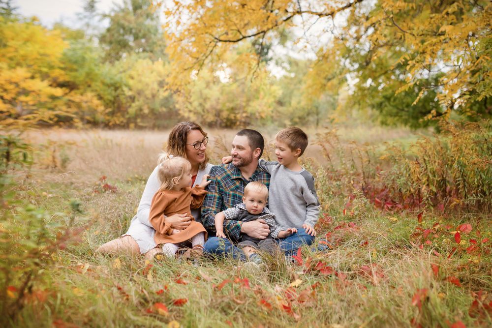 A family enjoys a warm autumn day sitting together in a field with golden foliage and red wildflowers.