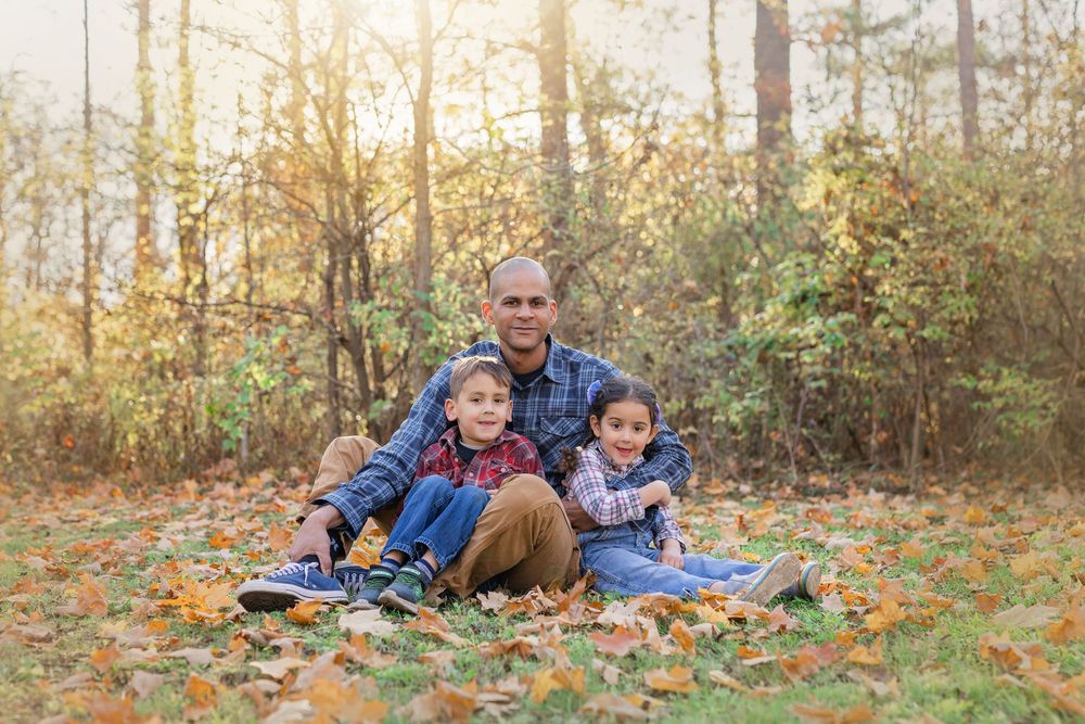 Family playing together outdoors in autumn leaves during golden hour sunset photo session at park.