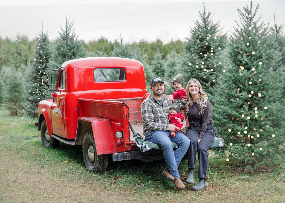 A red vintage pickup truck parked among evergreen Christmas trees at a tree farm during the holiday season.