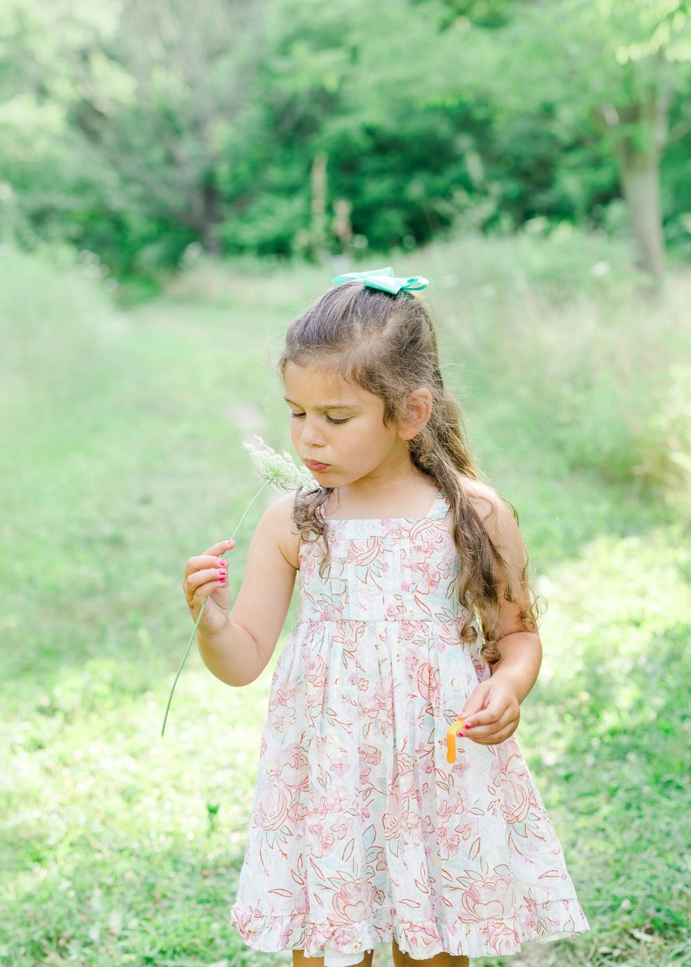A child in a floral print dress twirls playfully in a sunny green garden setting.