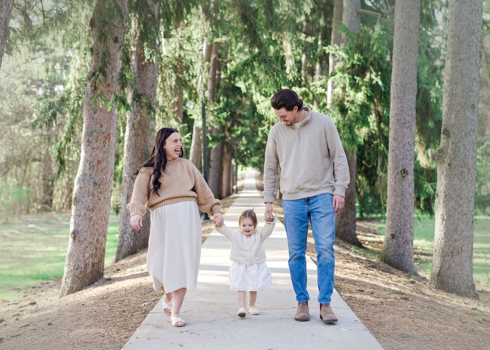 A couple walks together in a romantic forest setting with tall pine trees and sunlit pathways.