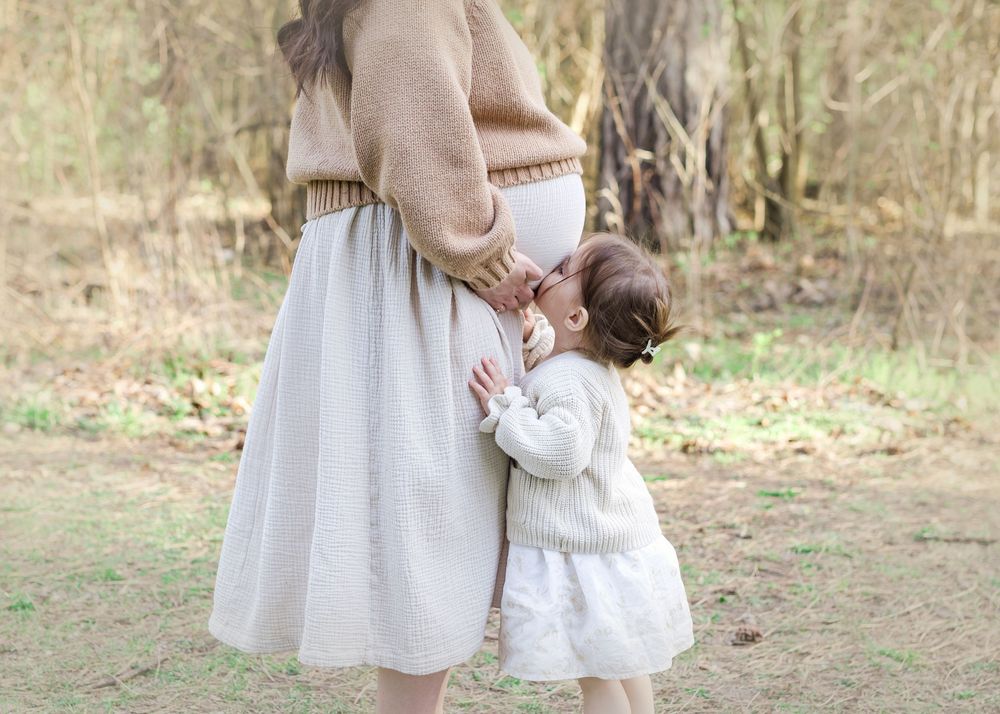 A tender moment between parent and child in matching white and beige outfits standing in a sunlit outdoor field.