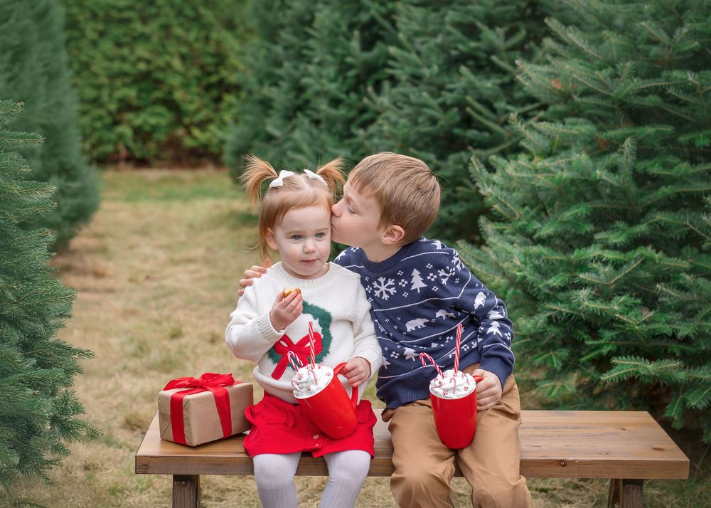 Family enjoying holiday moments at a Christmas tree farm with wrapped presents and festive decorations.