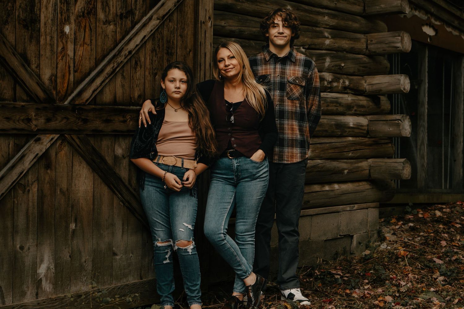 Three friends posing casually against rustic log cabin wall in autumn.
