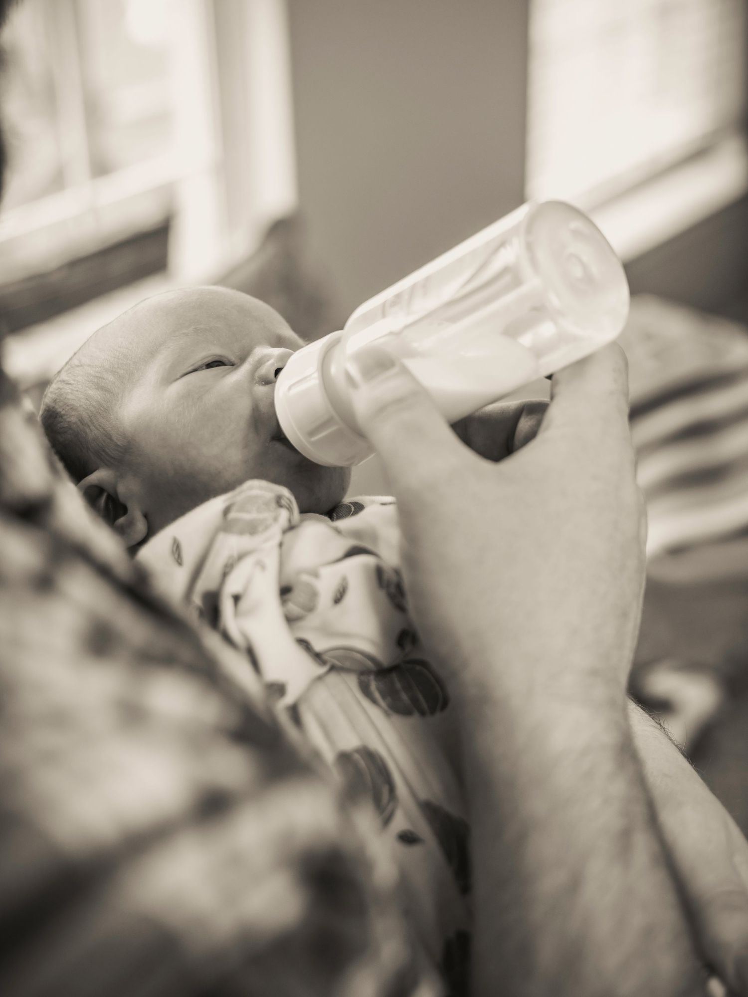 Black and white image of an infant being bottle fed in a tender moment.