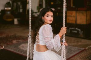 Person in white lace crop top sitting on a rustic rope swing.
