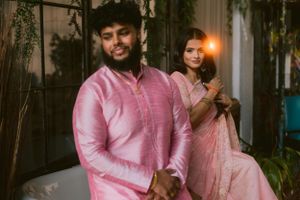 A couple wearing coordinated pink outfits pose together in an indoor garden setting.