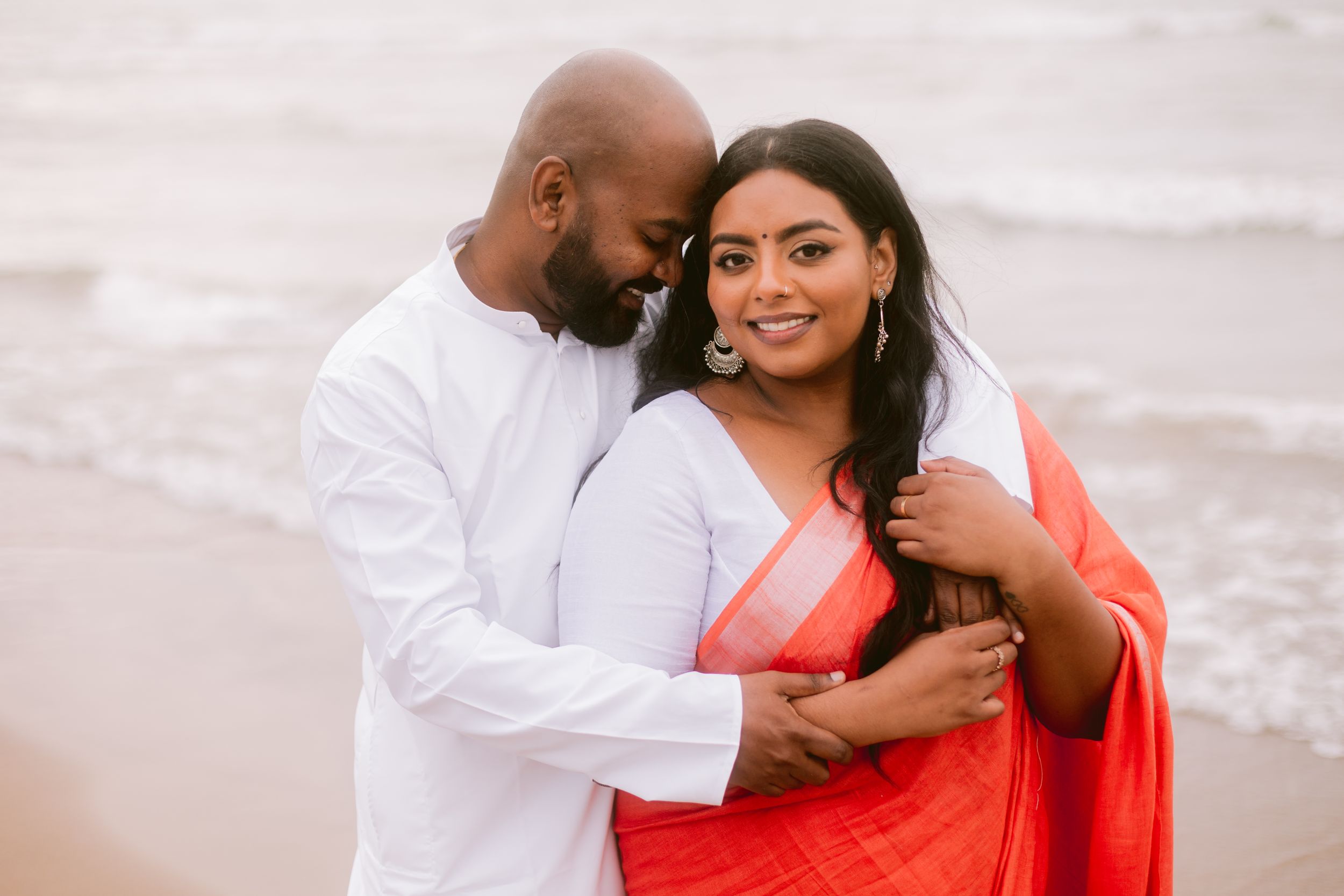 A romantic beach portrait of a couple in white and coral traditional attire.