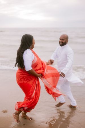 A playful couple in white and coral outfits dance in the ocean surf.