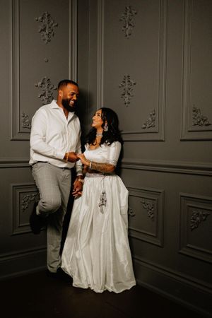 Couple sharing a joyful moment against an ornate gray wall during a romantic photoshoot.
