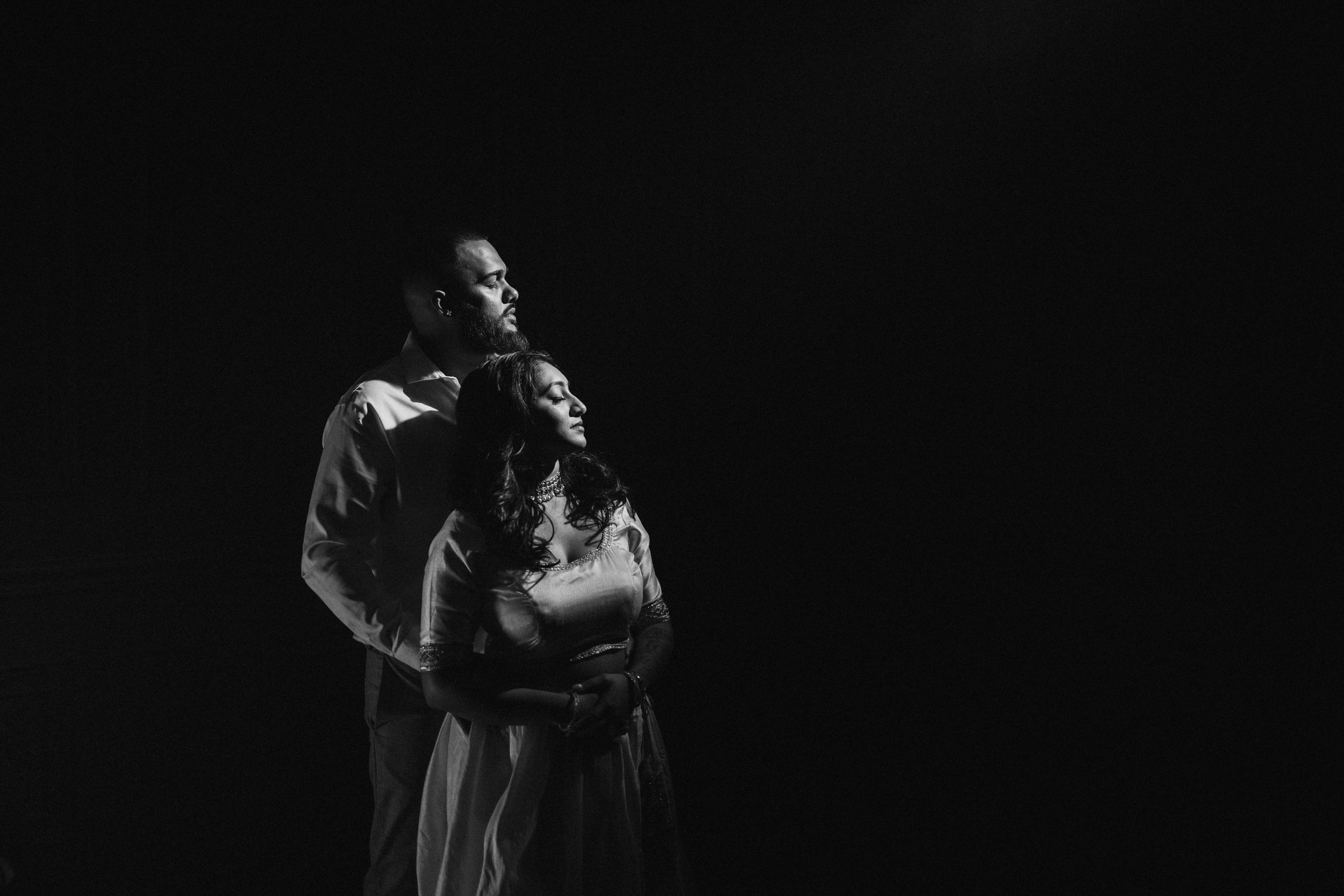 A dramatic black and white portrait of a couple in formal attire against a dark background.