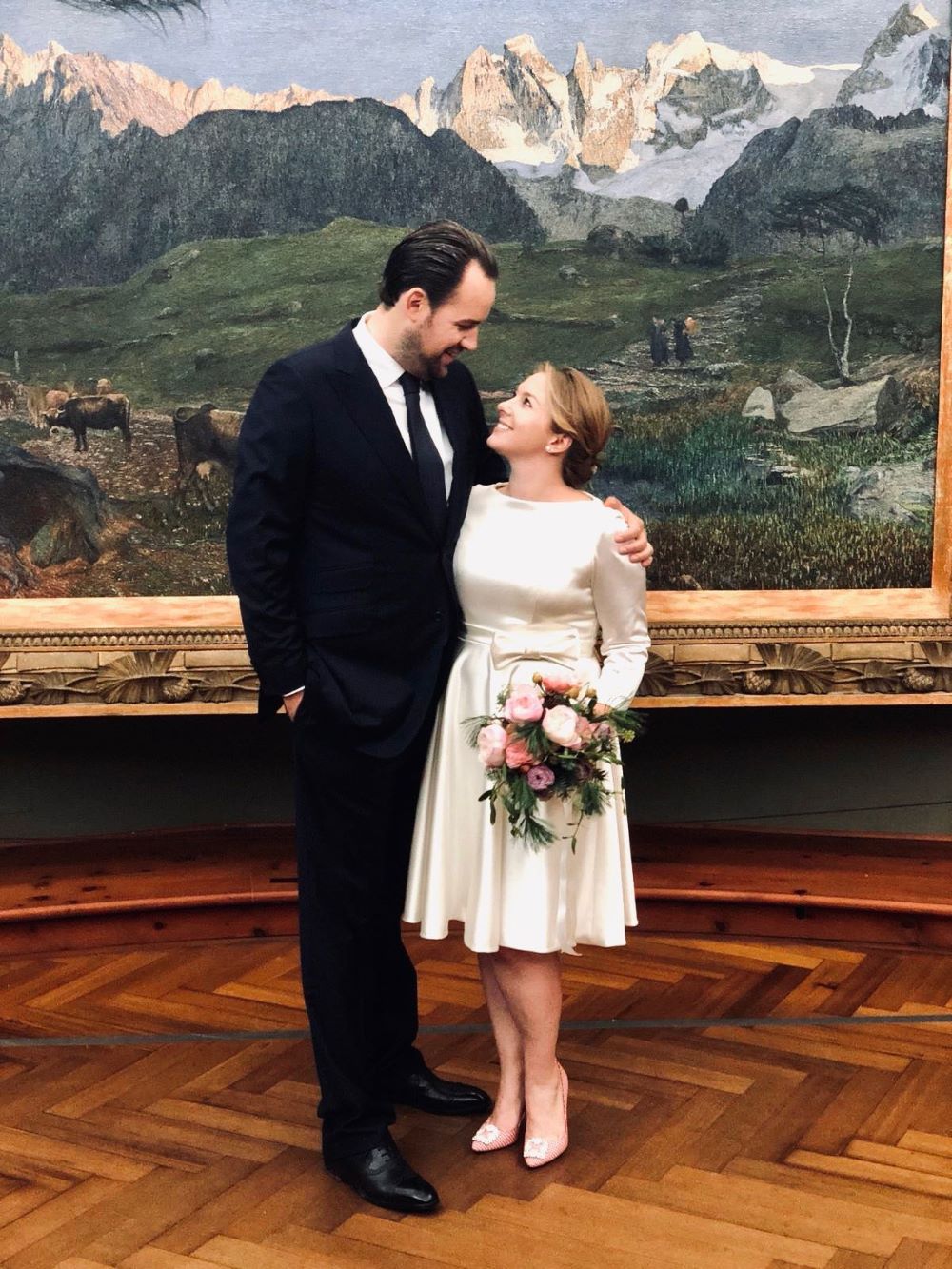 Brautpaar vor einem Gemälde. Die Braut trägt ein kurzes Seidenbrautkleid.