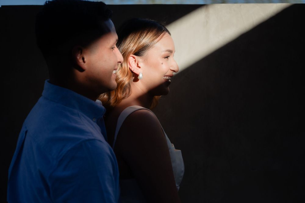Two people in profile standing together in dramatic side lighting against a dark background.