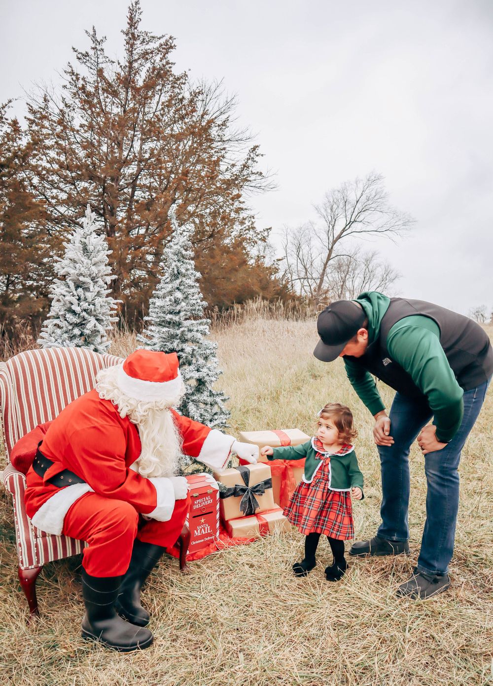 A festive outdoor Christmas scene with decorated trees and a striped armchair in a field.