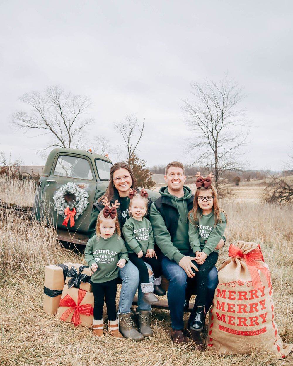A group poses on a vintage truck tailgate with holiday decorations and gift bags in a winter field setting.