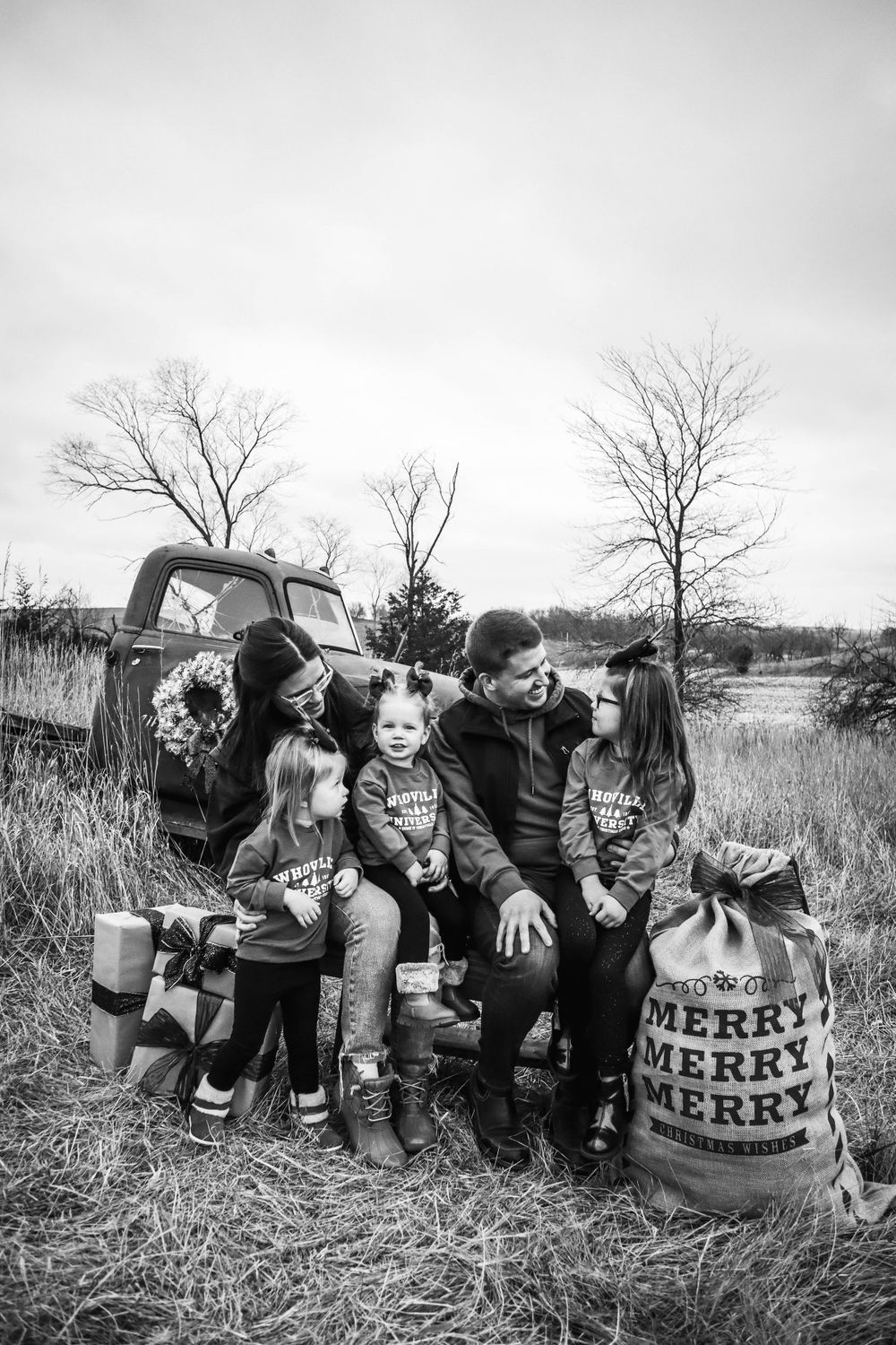 A black and white family portrait taken beside a vintage truck with Christmas decorations.