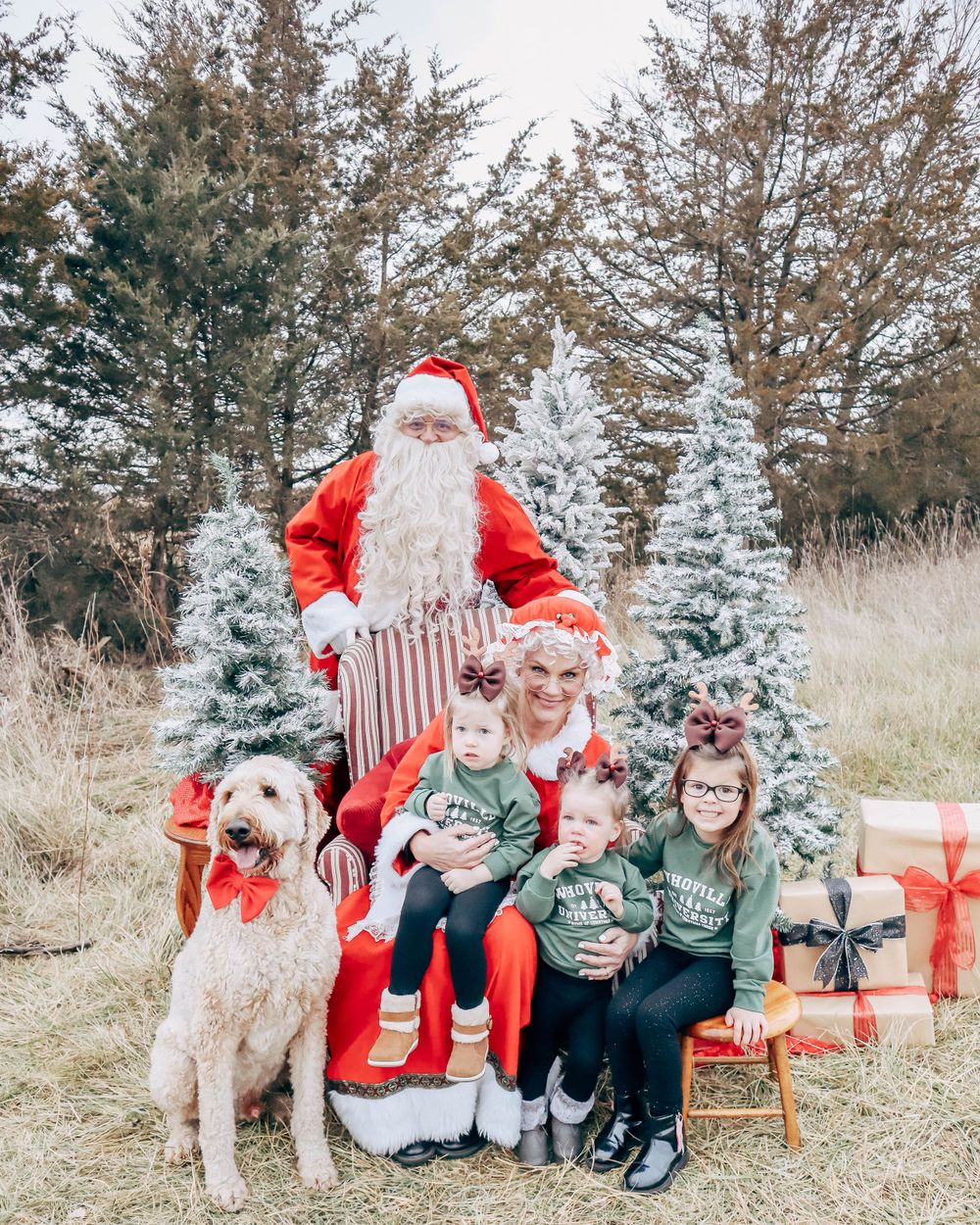 A holiday photo setup outdoors with decorated trees, presents, and a furry white dog.