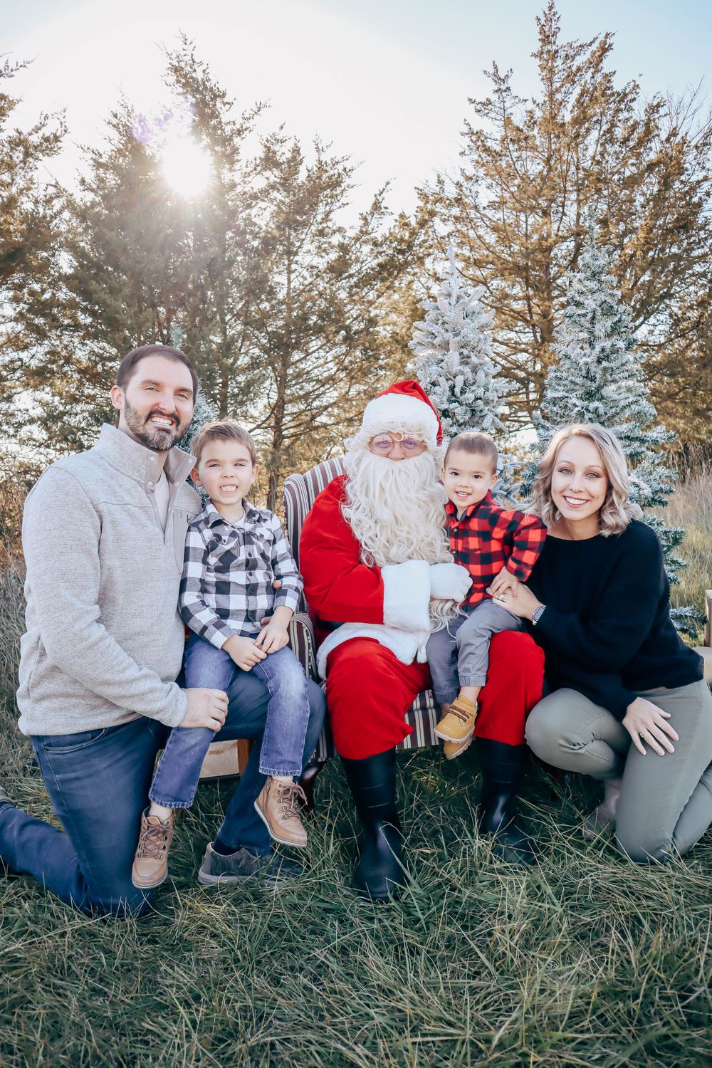 A festive outdoor photo shoot with Santa Claus and a family posed together among evergreen trees and snow.