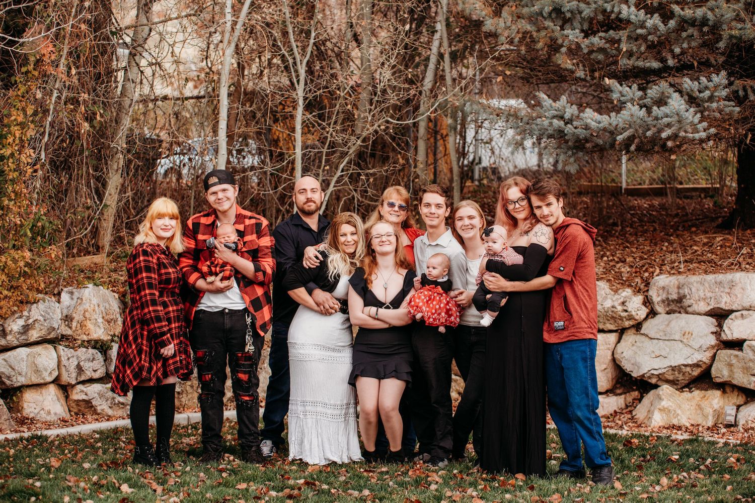 A group portrait of people in coordinating red and black outfits standing together against a stone wall in autumn.